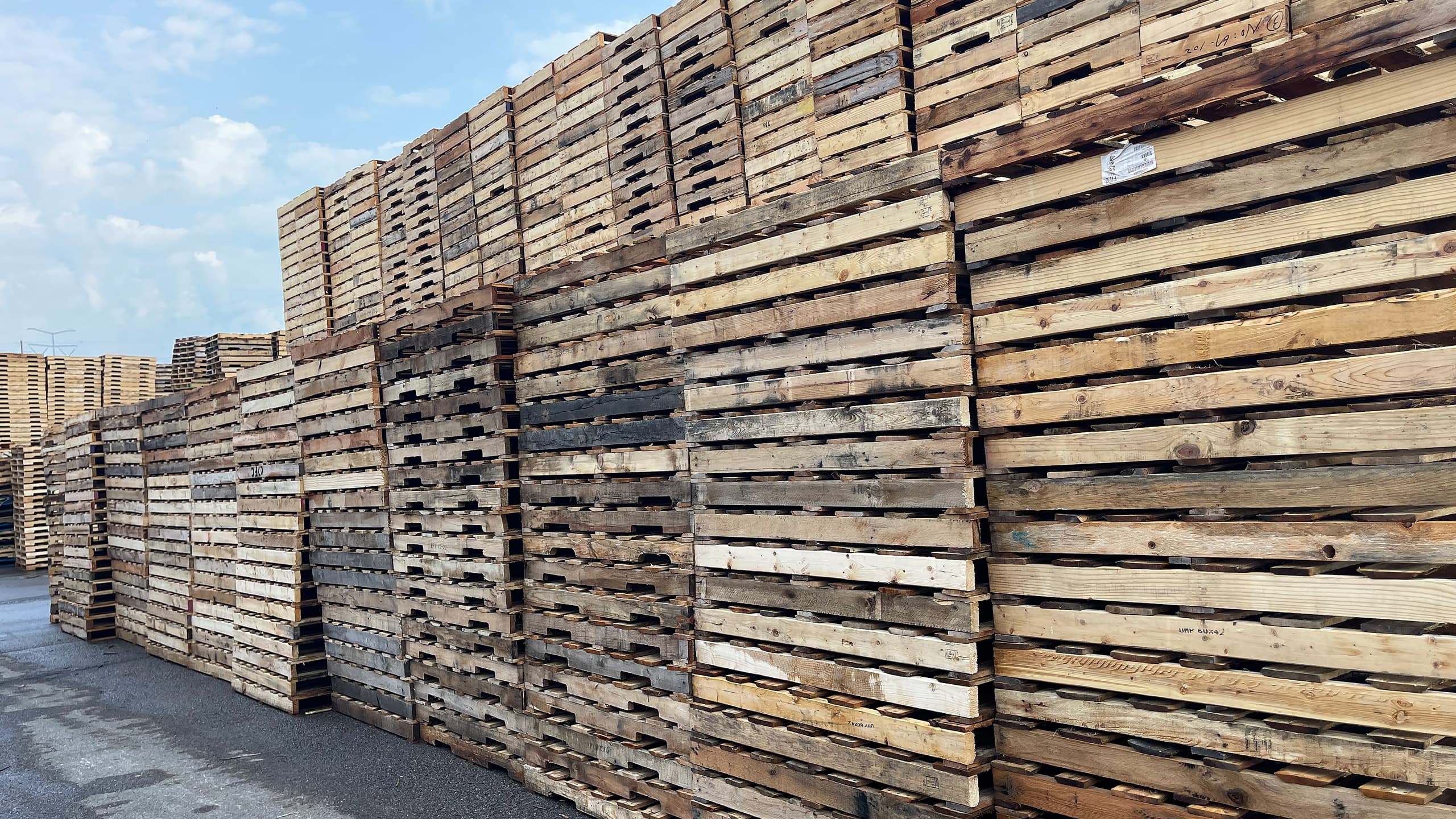 Remanufactured pallets arranged in stacks outdoors on a sunny day